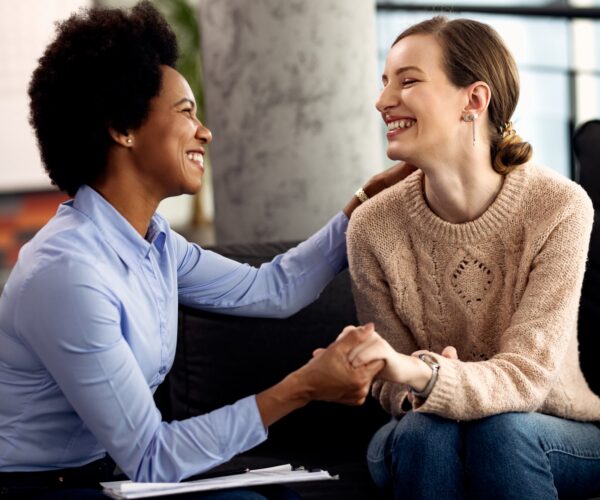 Young happy woman holding hands with her psychotherapist during an appointment at the clinic.